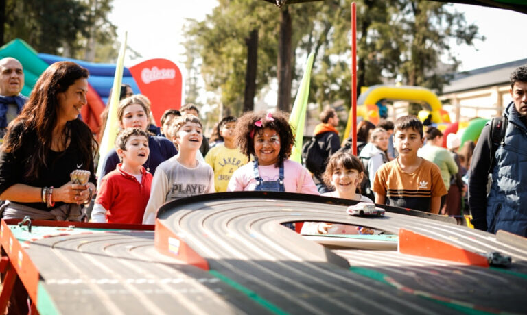 Esta imagen muestra un grupo de niños disfrutando de una pista de carreras de autos a escala durante una celebración del Día de las Infancias.